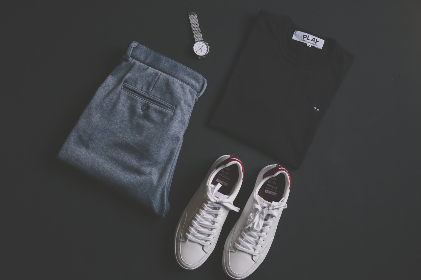 A real flat lay of sneakers, trousers, a shirt, and a watch.